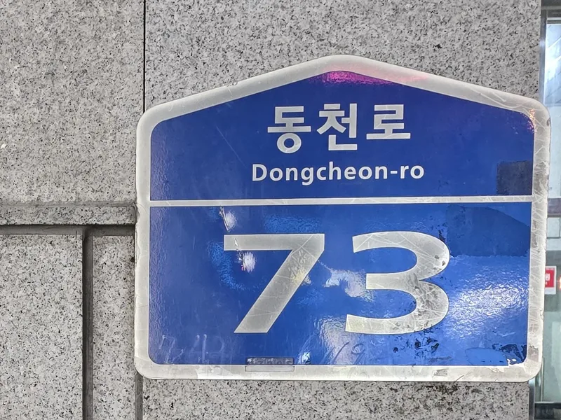 화강석 외벽에 붙은 파란 도로명판. 동천로 73