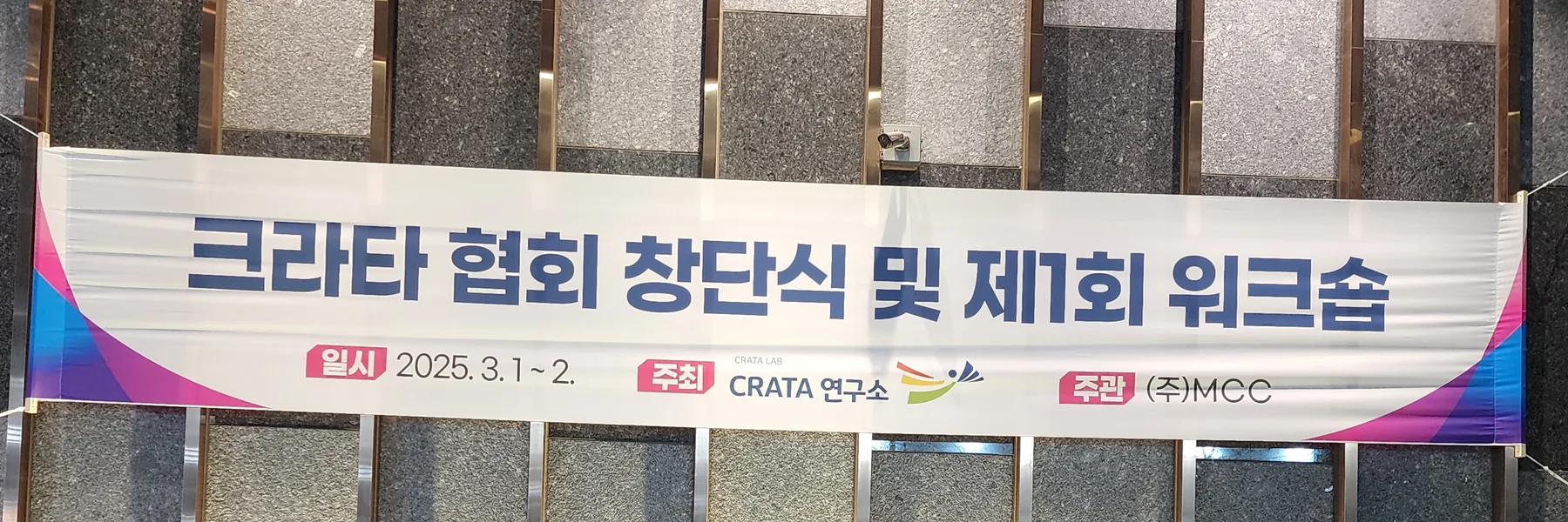건물 외벽에 걸린 행사 현수막. ‘크라타 협회 창단식 및 제1회 워크숍’, 일시 2025. 3. 1~2., 주최 CRATA 연구소, 주관 (주)MCC라고 적혀 있다