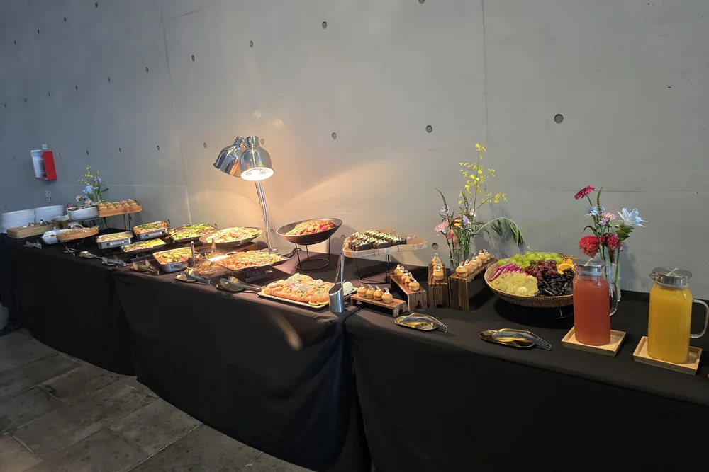 검은 천을 씌운 긴 테이블에 음식 접시와 과일, 주스를 담은 유리 피처, 꽃이 놓여 있다